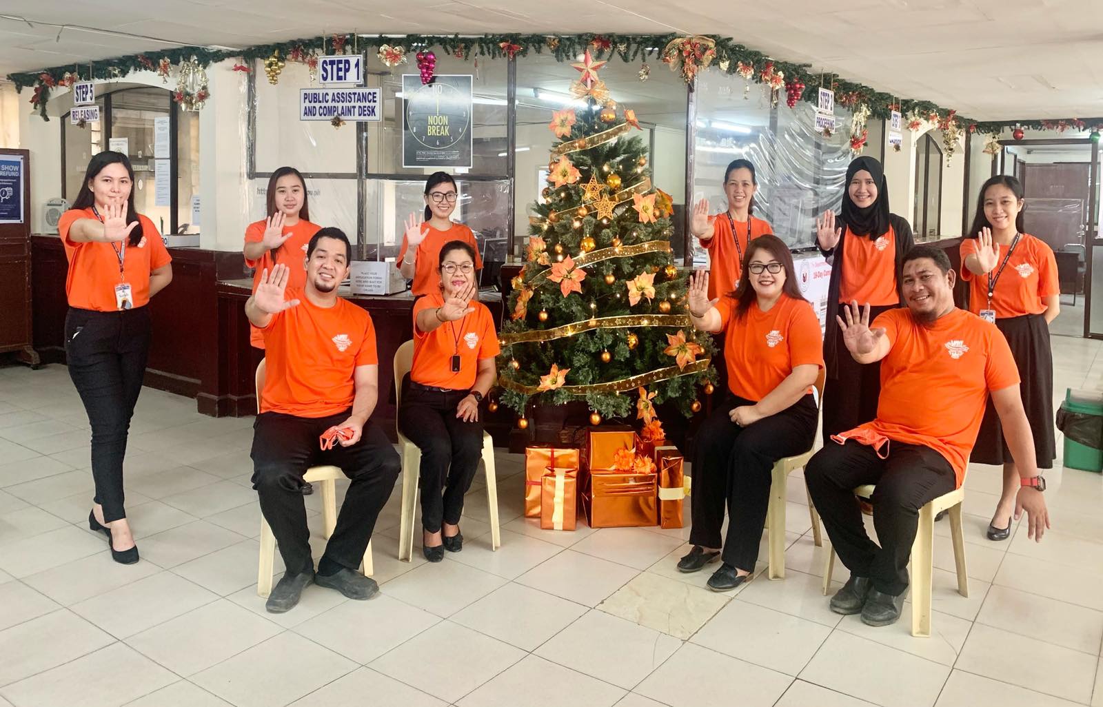 1 Consular personnel doing the Stop VAW hand sign while posing with the Christmas tree for the Orange your Icon campaign
